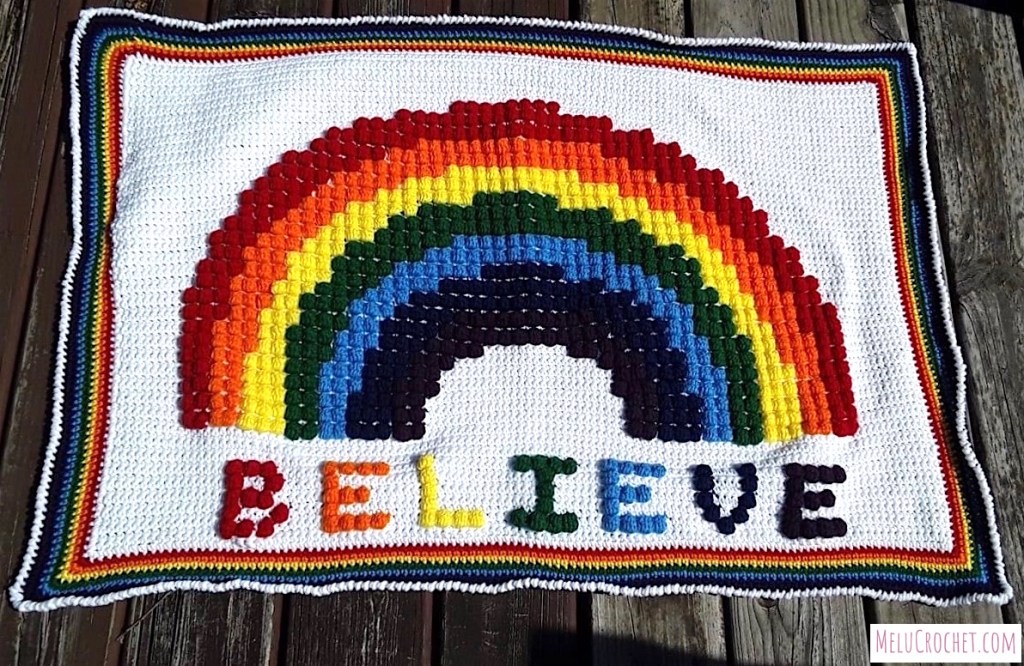 Crochet blanket with the word believe under a colourful rainbow