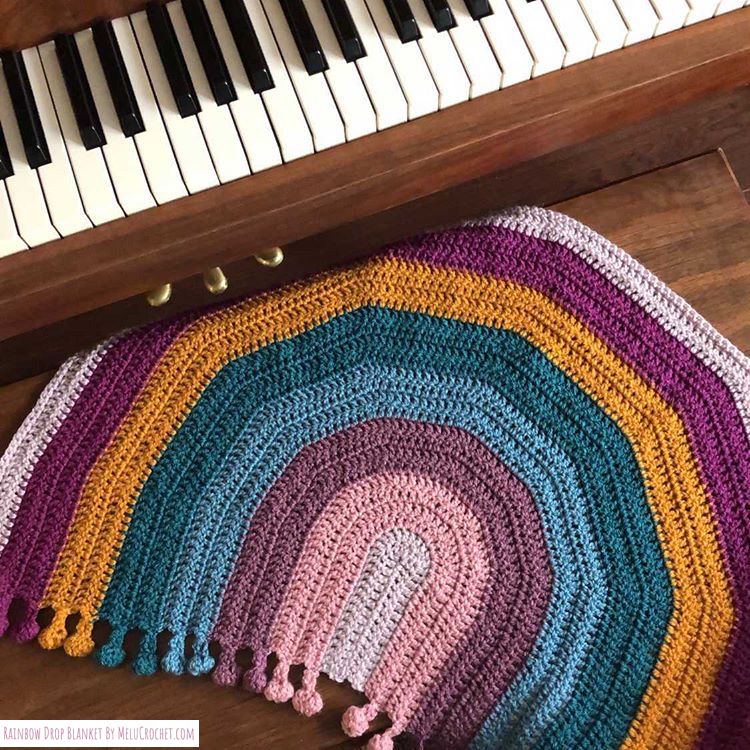 Rainbow shaped blanket with bobble pom pom fringe, beautifully styled with a piano