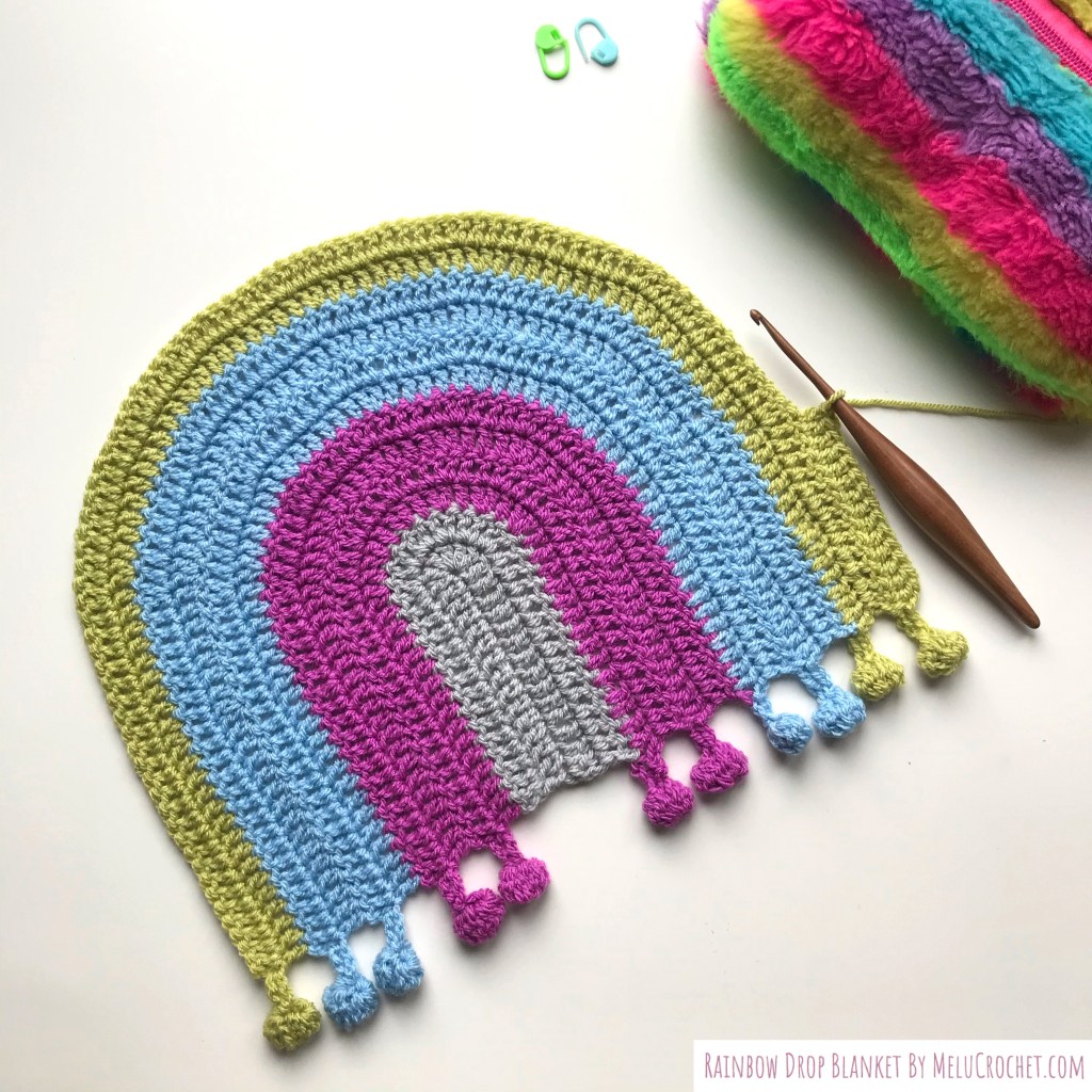 my Rainbow shaped blanket with bobble pom pom fringe in progress with furls crochet hook on the pistachio green round.